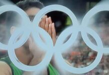 Paris 2024 Olympics: Javelin Throw Final | Pakistan’s Arshad Nadeem Wins World Record Gold A close-up photo of an athlete Arshad Nadeem with their hands covering their face, with the iconic Olympic rings blurred in the foreground. The image captures a moment of intense emotion during the Paris 2024 Olympics